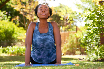 Beautiful young Black woman does upward facing dog yoga pose outdoors, trees