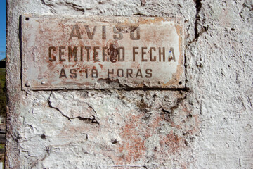 Placa antiga e enferrujada em parede de cemitério com o horário de funcionamento
