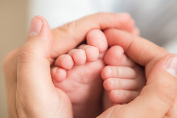 Loving mother holding in the hands feet of newborn baby. Baby feet in mother hands. Tiny Newborn Baby's feet on female hands closeup. Mom and her Child. Happy Family concept. Macro, close up