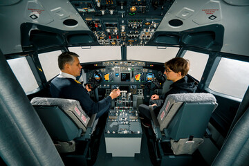 An experienced pilot instructs a young student before a training flight in the cockpit of an aero simulator