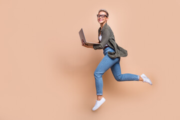 Full length photo of busy excited woman wear khaki shirt jumping typing emails gadget emtpy space isolated beige color background