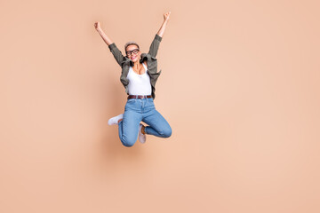 Full length photo of excited cool woman wear khaki shirt rising fists jumping high emtpy space isolated beige color background