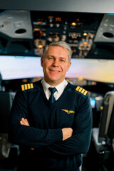 Portrait of smiling airplane captain in uniform preparing for flight in aero simulator cockpit