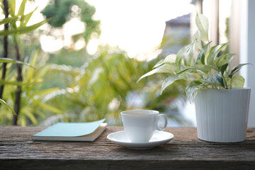 Blue notebook and wooden coffee cup and pothos plant pot on wooden table with greenery scene
