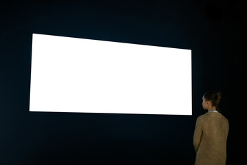 Woman looking at wide large wall blank interactive white display in dark room of modern technology...