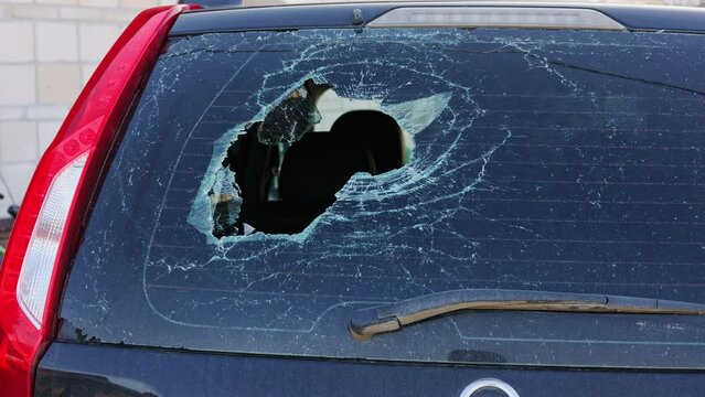 Broken glass in back door of car. Rear window of auto smashed on street by thief, hooligan, bandit. Automobile after road accident. Hole in damaged windshield of parked transport, vehicle