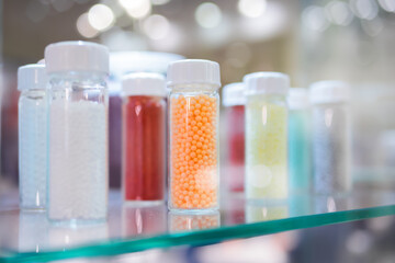 Plastic recycling, renewable resource - colorful secondary polystyrene, polyethylene, polypropylene granules or pellets in glass vessels at exhibition, trade show - close up