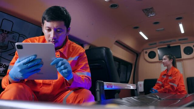 Emergency medical technician (EMT) Asian man or paramedic using tablet and sitting in ambulance car while the car was going to the emergency location and turned on the siren light