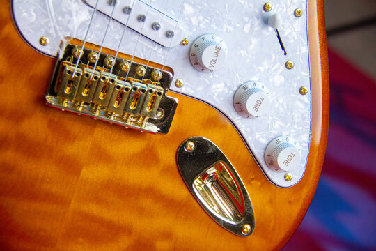 Close up of a solid orange electric guitar with single coil pickups, white pickguard and gold hardware.