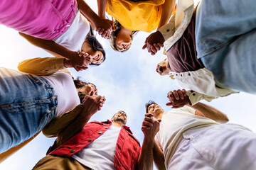 Low angle view of united group of young people in circle holding hands. Community, support and...