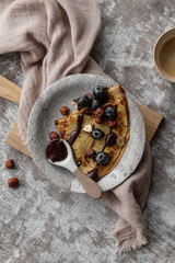 Crepes or blinis or thin pancakes with blueberries, hazelnuts and chocolate sauce on a white rustic...