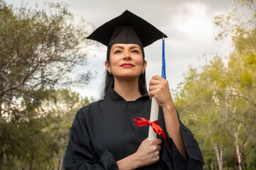 portrait of young female graduate in school cap and gown holding her degree outdoors