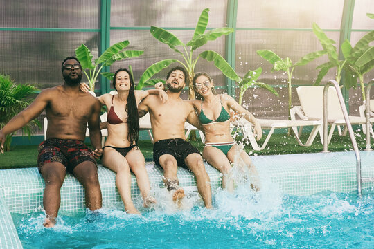 Summer vacation pool party: Group of friends having fun together inside luxury villa hotel - Multiracial people enjoy holiday weekend - Soft focus on center legs