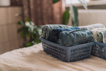 Folded jeans in a blue container on the bed.