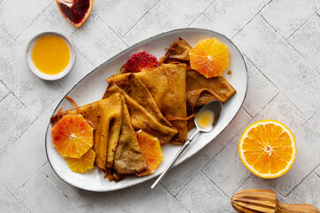 Traditional French Crêpes suzette pancakes with orange sauce on a serving dish on a light grey...