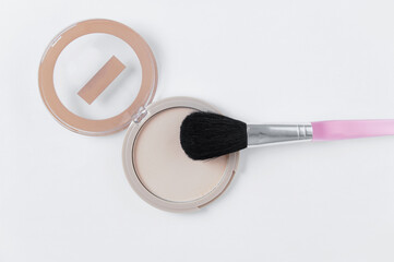 Compact face powder and cosmetic brush for applying powder. White background.