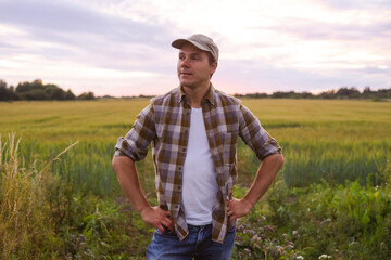 Naklejka na ściany i meble Farmer in front of a sunset agricultural landscape. Man in a countryside field. Country life, food production, farming and country lifestyle concept.
