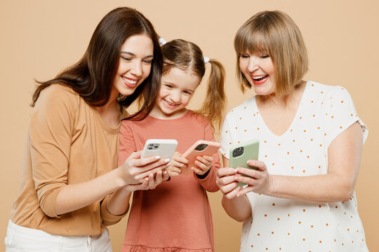 Happy Smiling Women Wear Casual Clothes With Child Kid Girl 6-7 Years Old. Granny Mother Daughter Hold In Hand Use Show Mobile Cell Phone Isolated On Plain Beige Background. Family Parent Day Concept.