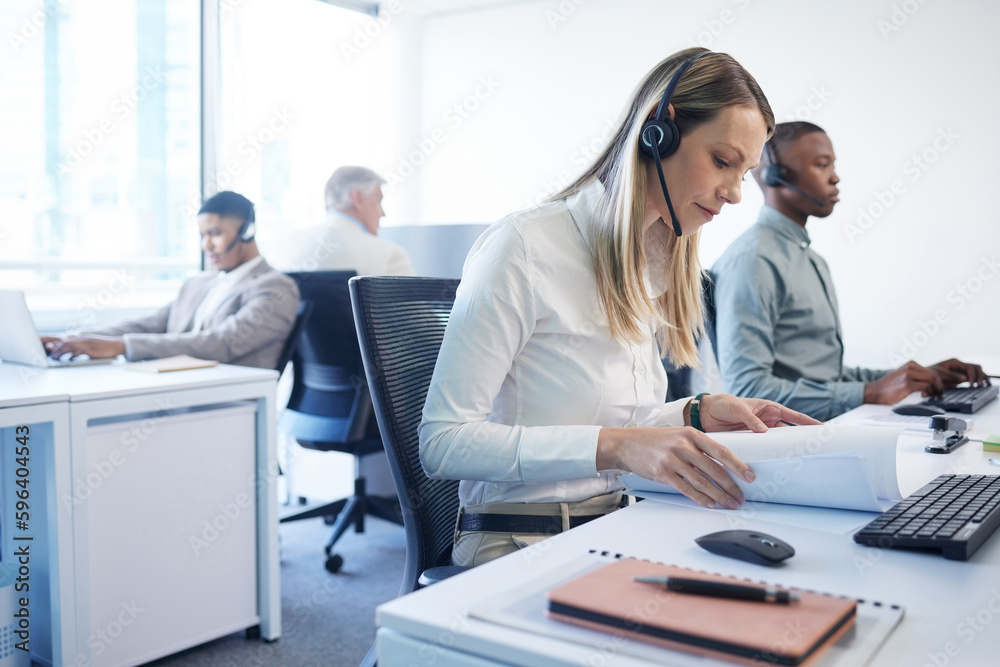 Wall mural Diligence gets it done. Shot of a mature businesswoman using a headset and going through paperwork in a modern office.