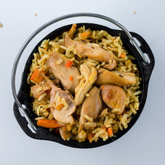 Hot pilaf with chicken meat, carrots, tomatoes, onions and herbs in a cast iron pot.