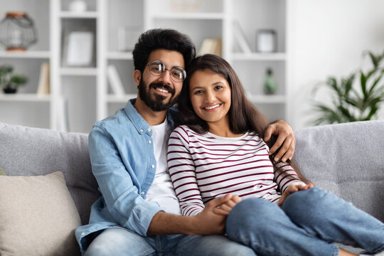 Portrait of cheerful eastern couple cuddling on couch at home