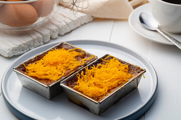 Coconut custard squares in Aluminium box food topping with Golden Egg strips in white plate (Khanom Maw Kaeng) ,Thai custard cake,tradition dessert