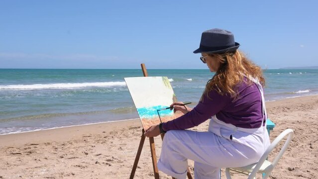 Lady painting a picture on the sand of the beach