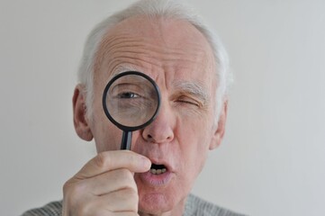 An elderly gray-haired man looks at something with a magnifying glass in amazement.