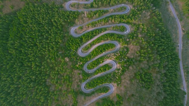 Aerial view of a winding road in the mountains shoot from a drone while flying backwards. The video was shoot with the camera tilted downwards for a top view of the serpentines and the traffic.