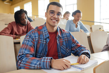 Portrait of schoolboy in eyeglasses smiling at camera while sitting at desk at lecture