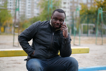 African american man sits at sport ground and speaks on smartphone