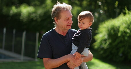 Grand-father holding one year old baby infant toddler in arms outdoors