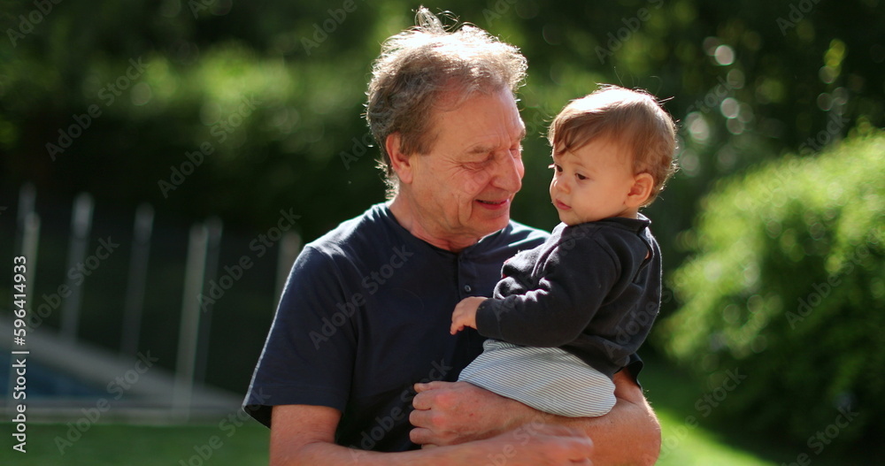 Wall mural grand-father holding baby infant in arms outside in backyard. grand parent bonding with grand-child