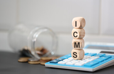 A sigla ICMS escrita em dados de madeira que estão sobre uma calculadora. Um pote de vidro com moedas do Brasil na composição. - obrazy, fototapety, plakaty