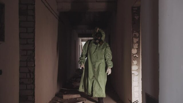 A man in a protective suit and a gas mask walking in the corridor of abandoned building