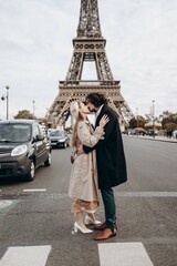 A couple in love walks along the streets of Paris, a guy in a coat and a suit, a girl in a dress with a beret and a trench coat in autumn