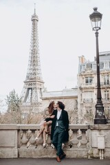 A couple in love walks along the streets of Paris, a guy in a coat and a suit, a girl in a dress with a beret and a trench coat in autumn