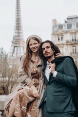 Fototapeta premium A couple in love walks along the streets of Paris, a guy in a coat and a suit, a girl in a dress with a beret and a trench coat in autumn