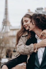Fototapeta premium A couple in love walks along the streets of Paris, a guy in a coat and a suit, a girl in a dress with a beret and a trench coat in autumn