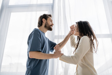 Low angle view of angry woman holding hands of boyfriend and quarrelling at home.