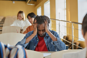 African American schoolboy holding his head having headache while sitting at desk during exam