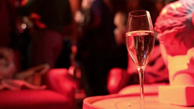 A glass of champagne on the table against the backdrop of dancing people in a nightclub