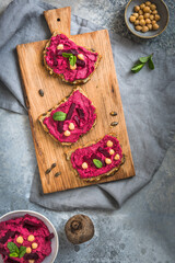Fototapeta na wymiar Wooden board of bread slices with beetroot hummus on a gray background, top view
