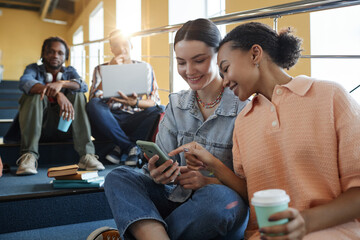 Group of students chatting and using gadgets while resting during break at college
