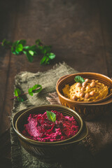 Bowls with beetroot hummus and chickpea hummus on a rustic dark wooden background, vertical with copy space