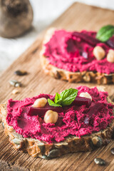 Wooden board of bread slices with beetroot hummus on a white wooden background, vertical