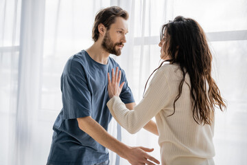 Brunette woman pushing angry boyfriend during conflict at home.