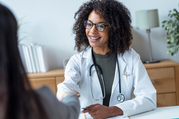 Beautiful cheerful female doctor talking while explaining medical treatment to patient in the...