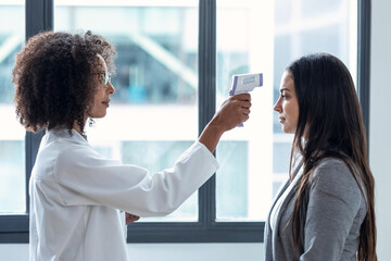 Cheerful beautiful female doctor taking woman patient temperature with thermometer in medical consultation