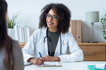 Beautiful cheerful female doctor talking while explaining medical treatment to patient in the...